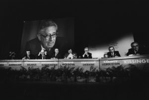 reunión WEF con Kissinger en segundo plano en pantalla gigante